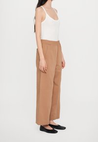Brązowe spodnie typu wide-leg z elastycznym paskiem w talii, w zestawie z białym topem na ramiączkach i czarnymi balerinkami. Gładki, teksturowany materiał z bocznymi kieszeniami.