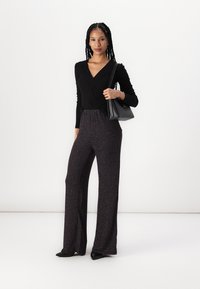 Black long-sleeve top with a V-neck, paired with wide-leg textured pants in dark colors and subtle patterns, accessorized with a black bag.
