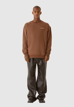 Brun sweatshirt med rund hals og hvid tekst. Kombineret med løse sorte skinnende bukser og sorte sko. Glat stof og afslappet pasform.