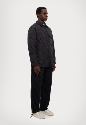 Padded black quilted jacket with a collared design, front pocket, and snap buttons, paired with black cargo pants and beige sneakers.