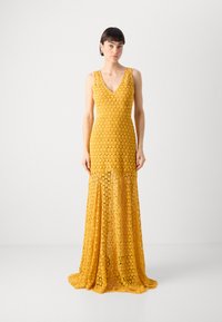 Gul blomstret lace kveldskjole med V-hals, uten ermer, tettsittende liv, og flytende skjørt som ender i en subtil tog.