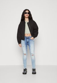 Svart bomberjakke, grønn kort topp, lyseblå slitte skinny jeans og svarte joggesko med gule detaljer. Brukt med solbriller.