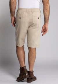 Beige šortky s elastickým pasem, dvěma zadními kapsami s knoflíky a rovný střih. Nosené s hnědými koženými botami.