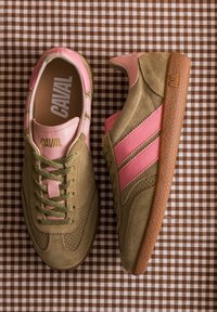 Paire de baskets en daim marron et rose avec des lacets verts sur une surface en tissu à carreaux marron et blanc.