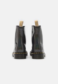 Botines de charol negro con costuras amarillas y lengüetas para tirar, con un acabado liso y brillante y un diseño de punta redonda.