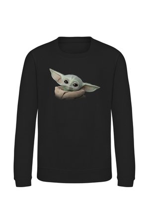Sort langærmet skjorte med en grafik af en lille grøn rumvæsenbaby med store ører, indpakket i et beige klæde på brystet.