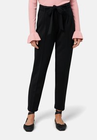 Czarne, dopasowane spodnie z wysokim stanem, z przodu ozdobione kokardą, bocznymi kieszeniami i gładkim materiałem. Połączone z różowym, prążkowanym swetrem.