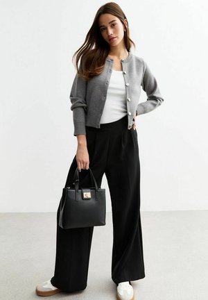Cardigan en tricot gris avec col rond et fermeture à boutons, associé à un haut blanc et un pantalon large noir. Sac à main noir avec accents dorés.