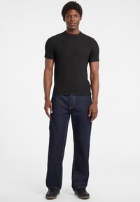 Czarny prążkowany t-shirt z krótkim rękawem zestawiony z granatowymi dżinsami o prostym kroju. Outfit uzupełniają czarne trampki z szarymi podeszwami.