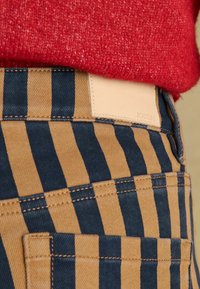 Pantaloni cu dungi în culorile bleumarin și bej, confecționați din denim, cu o etichetă din piele bej inscripționată "JOULES" pe talie. Cusături texturate vizibile.