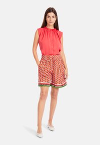 Red sleeveless blouse with gathered neckline paired with vibrant orange shorts featuring a fruit print and decorative trim.