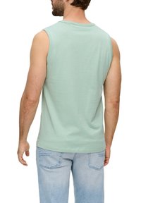 Mintgrünes, ärmelloses Shirt aus weichem Baumwollmaterial mit Rundhalsausschnitt und lockerer Passform, kombiniert mit hellblauen Jeans.