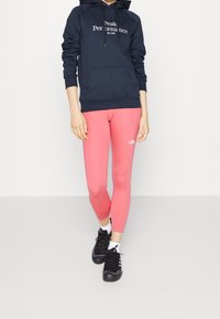 Felpa navy con logo bianco, abbinata a leggins rosa con logo e scarpe da ginnastica nere. Tessuto morbido, design aderente.