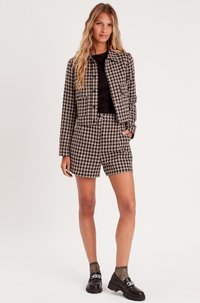 Veste à carreaux et shorts en motif pied-de-poule noir et blanc. Le matériau semble texturé. Un haut noir, des chaussures noires et des chaussettes grises complètent l'ensemble.