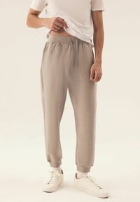 Helle graue Jogginghosen aus weichem Stoff, mit elastischem Bund und Kordelzug, Seitentaschen und gerippten Bündchen, kombiniert mit weißen Sneakern.