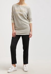 Top beige de manga larga a rayas con escote redondo y texto dorado, combinado con pantalones negros ajustados y zapatillas blancas. Diseño sencillo.