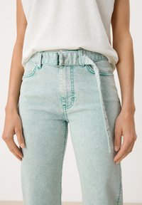 Jeans de tiro alto en verde menta claro con un ajuste relajado, que presentan un cinturón con una hebilla plateada y costuras en contraste a lo largo de las costuras.