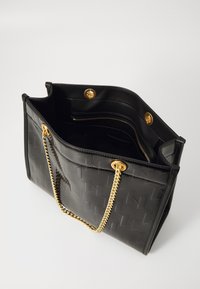 Borsa a tote nera in finta pelle con una trama intrecciata, spallacci in catena dorata e chiusura a bottone. L'interno presenta tasche con zip e tasche a soffietto.