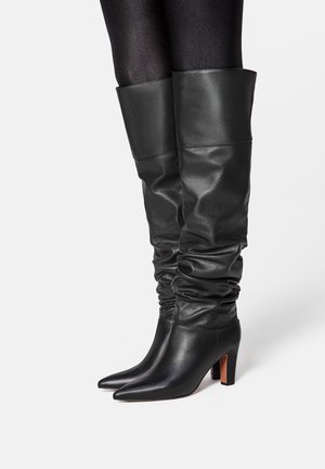 Black leather knee-high boots with a slouchy design, pointed toe, and chunky heel. Smooth texture with a shiny finish and folded top.
