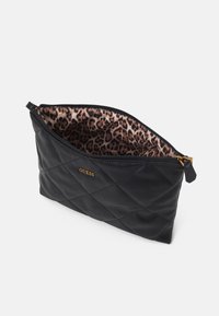Pochette noire matelassée avec logo Guess doré et intérieur en tissu imprimé léopard, partiellement dézippée montrant la doublure intérieure.