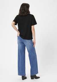 Tricou negru cu mânecă scurtă, asortat cu blugi albaștri cu talie înaltă și picior larg, purtat cu cizme negre cu toc. Design simplu, fără modele sau logo-uri.