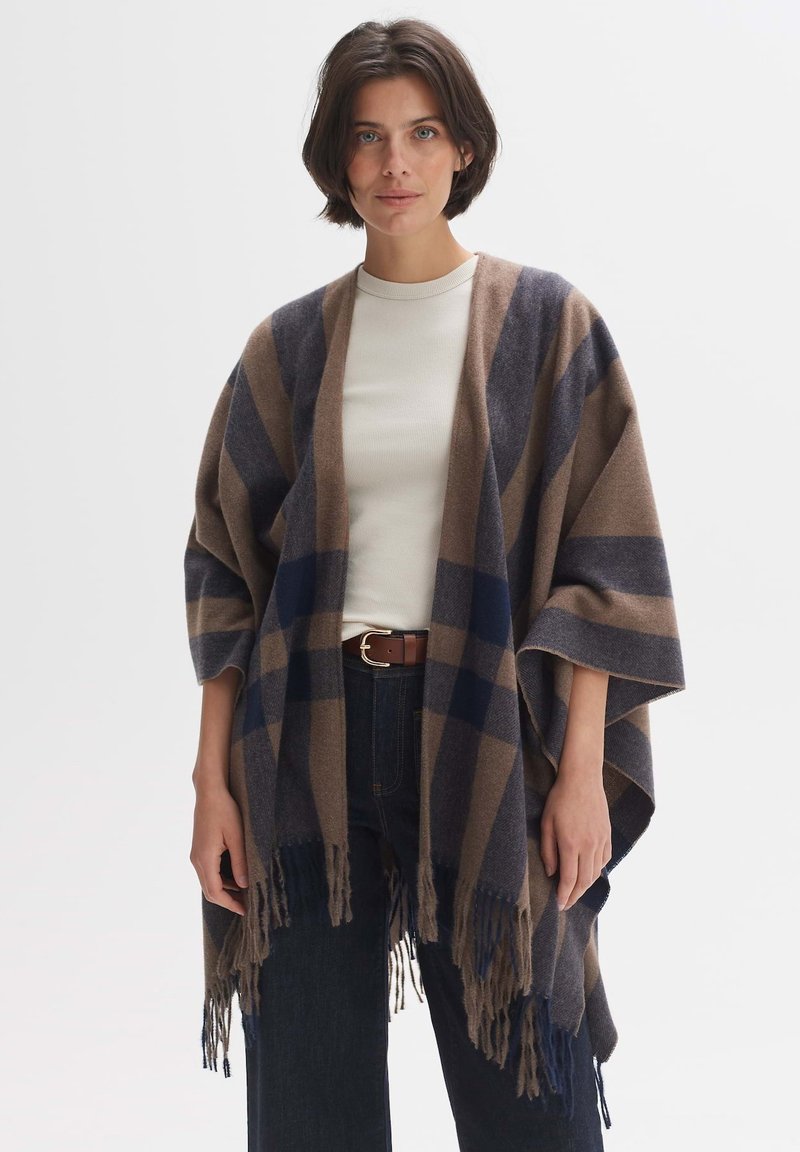 Oversized brown and navy checked poncho with fringe trim, made of soft fabric, features wide sleeves and an open front design.