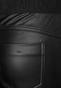 Černé kožené kalhoty s texturovaným povrchem, úzkým střihem a detaily na zadní kapse s viditelným prošíváním a páskem se zlatým ražením.