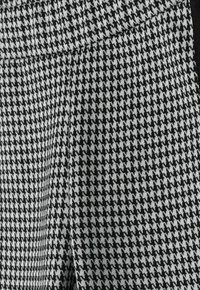 Črno-bele tkanine s houndstooth vzorcem in teksturirano površino, ki vsebuje gladek pas in subtilne detajle šivov.