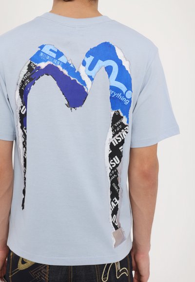 Light blue cotton t-shirt featuring a large graphic of torn blue and black layered designs on the back, creating an abstract shape.