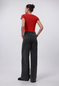 Un crop top rouge à côtes associé à un pantalon en denim gris foncé à taille haute et jambes larges, doté d'une taille élastique et de poches arrière.