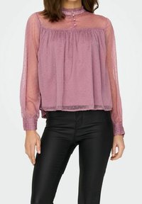 Blouse prune transparente à motif à pois, col rond, boutons sur le devant, taille froncée et manches longues bouffantes, associée à un pantalon en cuir noir.