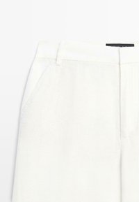 White high-waist pants with belt loops and slanted front pockets, showing upper section and waistband details.