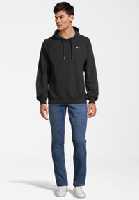 Felpa nera in pile con cappuccio e cordini, logo sul petto, abbinata a jeans in denim blu e sneakers bianche. Design semplice e forma aderente.