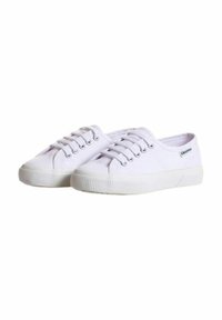 Sneakers bianchi in tela con punta arrotondata, design con lacci, suola in gomma testurizzata e branding minimale sul lato.