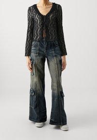 Svart spetskort cardigan med V-hals och bandknoppsstängning, kombinerad med ljus tvätt, vida cargojins med sidofickor.