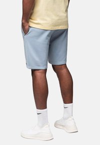 Shorts de sport bleu clair avec une taille élastique, des poches latérales et une texture lisse, associés à des sneakers et des chaussettes blanches.