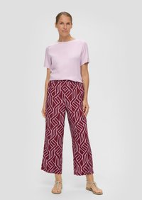 Lila korte mouwen top en kastanjebruine wijde broek met ingewikkelde witte geometrische patronen. Model draagt decoratieve sandalen.