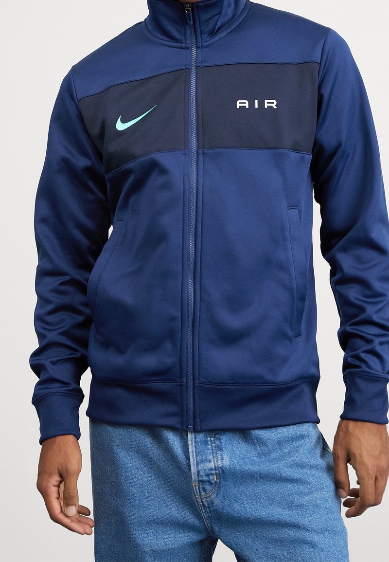 Mörkblå Nike zip-up-jacka med "AIR"-logotyp i vitt. Har en enfärgad design, två fickor och ribbade mudd för en välsittande look.