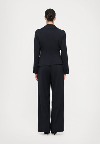 Marineblå skræddersyet blazer med en tætsiddende talje, ledsaget af brede bukser. Glat stof, knapper på ærmerne og en klassisk spids krave.