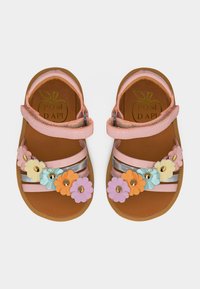 Παιδικά ροζ σανδάλια με ρυθμιζόμενους ιμάντες και πολύχρωμες διακοσμήσεις λουλουδιών μπροστά σε καφέ σόλες.