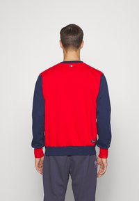 Sweatshirt bicolore rouge et marine avec un col rond, des poignets et une ceinture côtelés ; comporte un logo sur l'ourlet et à la nuque.