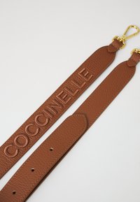 Ruskea nahkavyö, jossa on kohokuvioitu "COCCINELLE" -logo, teksturoitu pinta, säädettävät reiät ja kultainen kiinnike.
