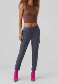 Grå skräddarsydda byxor med en slät textur, ihop med en figurnära brun ribbad crop top och livliga rosa klackstövlar.