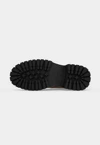 Semelle de bottes noire avec de profondes rainures, des motifs de grip en forme de croix au centre et des bords texturés pour une meilleure adhérence.