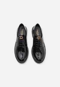 Chaussures à lacets en cuir noir brillant avec des clous dorés et un détail de boucle dorée sur le dessus, marque étiquetée Twinset Milano à l'intérieur.