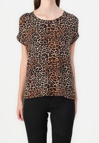 Top à imprimé léopard en orange, noir et crème ; manches courtes ; col rond ; coupe loose, fabriqué en tissu léger. Associé à un pantalon noir.