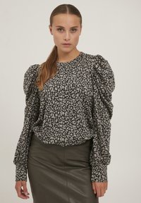 Bluse med sort og hvidt mønster, puffede ærmer, rund halsudskæring og løs pasform, parret med et mørkt læderskirt.