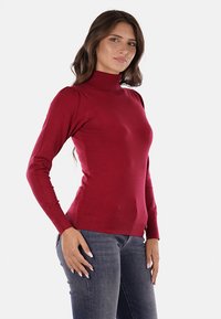 Maglione a collo alto rosso realizzato in un tessuto morbido e leggero. Presenta maniche lunghe con polsini a coste e un design aderente.
