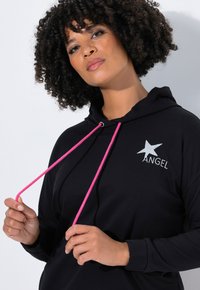 Zwarte hoodie met roze trekkoord en een zilveren ster met de tekst "ANGEL" gedrukt op de voorkant. Zachtheid van het materiaal en een ontspannen pasvorm.