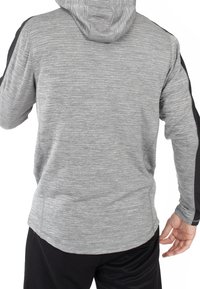 Felpa sportiva grigia con tessuto texturizzato; presenta pannelli laterali neri e un cappucci. La lunghezza è fino ai fianchi, con maniche lunghe e una vestibilità comoda.